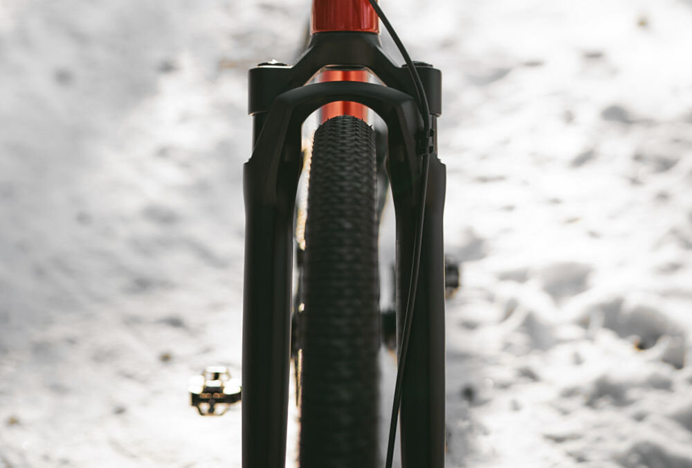 Rower gravel ROMET NYK 3.0 SRAM 28580365-A U23 28 cali męski Czerwono-czarny zimowa sceneria rower widoczny od przodu ustawiony na śniegu w lesie zbliżenie na amortyzator przedni amortyzator Rock Shox Rudy tapered z goleniami o średnicy 30 mm pomaga tłumić drgania i wstrząsy ręce i nadgarstki są mniej obciążone większa kontrola