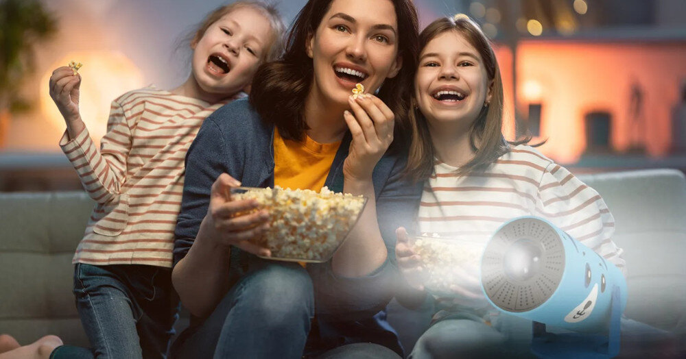 Trzy osoby siedzą na kanapie, jedząc popcorn i oglądając film. Obok nich znajduje się niebieski projektor z włączonym światłem.