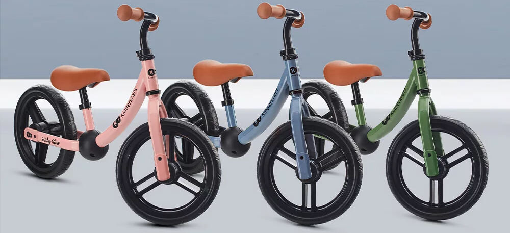 Rowerek biegowy 2WAY NEXT 2022 BLUE niebieskie tło trzy rowerki różowy niebieski i zielony brązowe siodełka gumowe uchwyty funkcjonalność estetyka subtelne pastelowe barwy stylowe wzornictwo brak ostrych krawędzi zaokrąglona konstrukcja precyzyjne wykonanie praktyczny pojazd urocza zabawka 