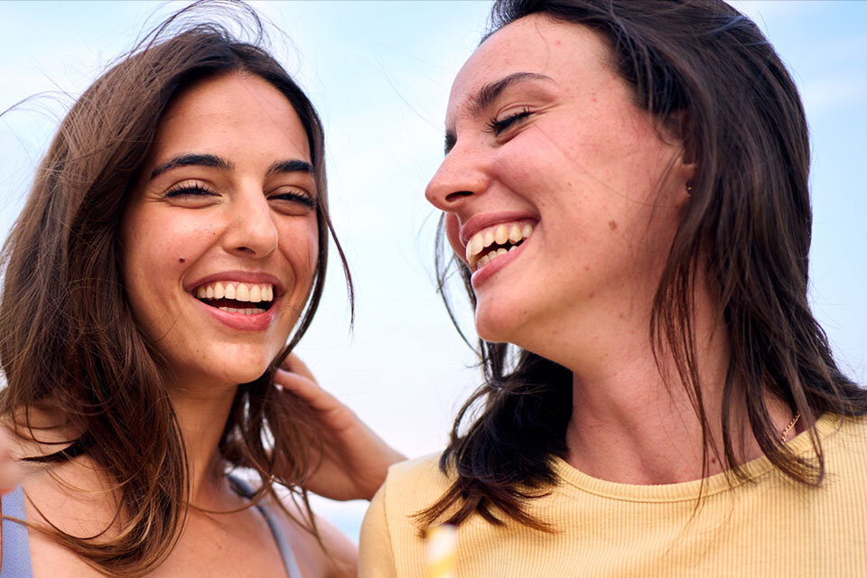 Dwie osoby stoją blisko siebie na zewnątrz. Jedna ma na sobie jasnoniebieski bezrękawnik, druga żółtą koszulkę z krótkim rękawem. Podkreśla to funkcjonalność Super HDR w Galaxy S25 FE.