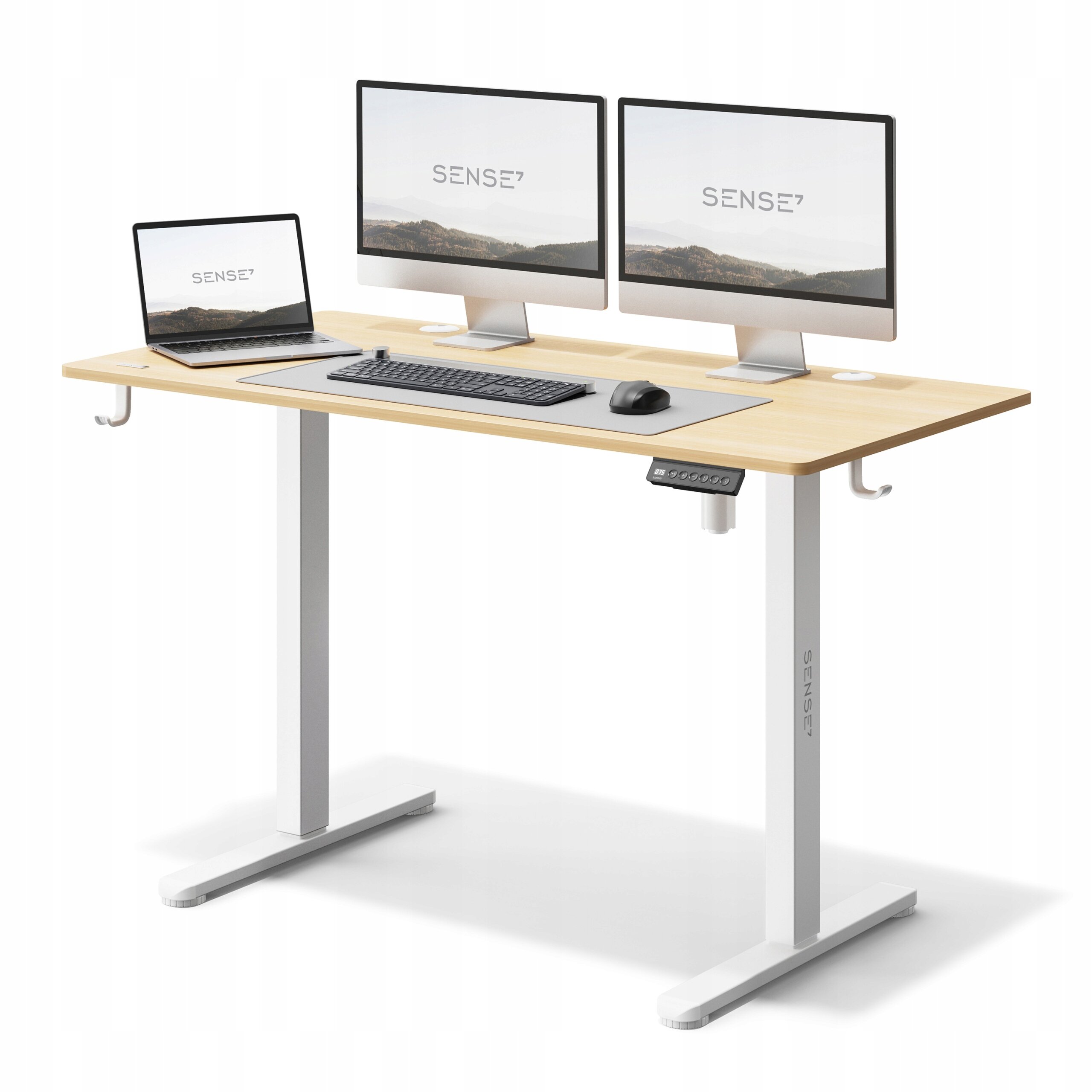 Biurko z jasnobrązowym blatem i białymi nogami, wyposażone w dwa monitory, laptop, klawiaturę i myszkę. Na blacie widoczne jest logo \'SENSE7\'.
