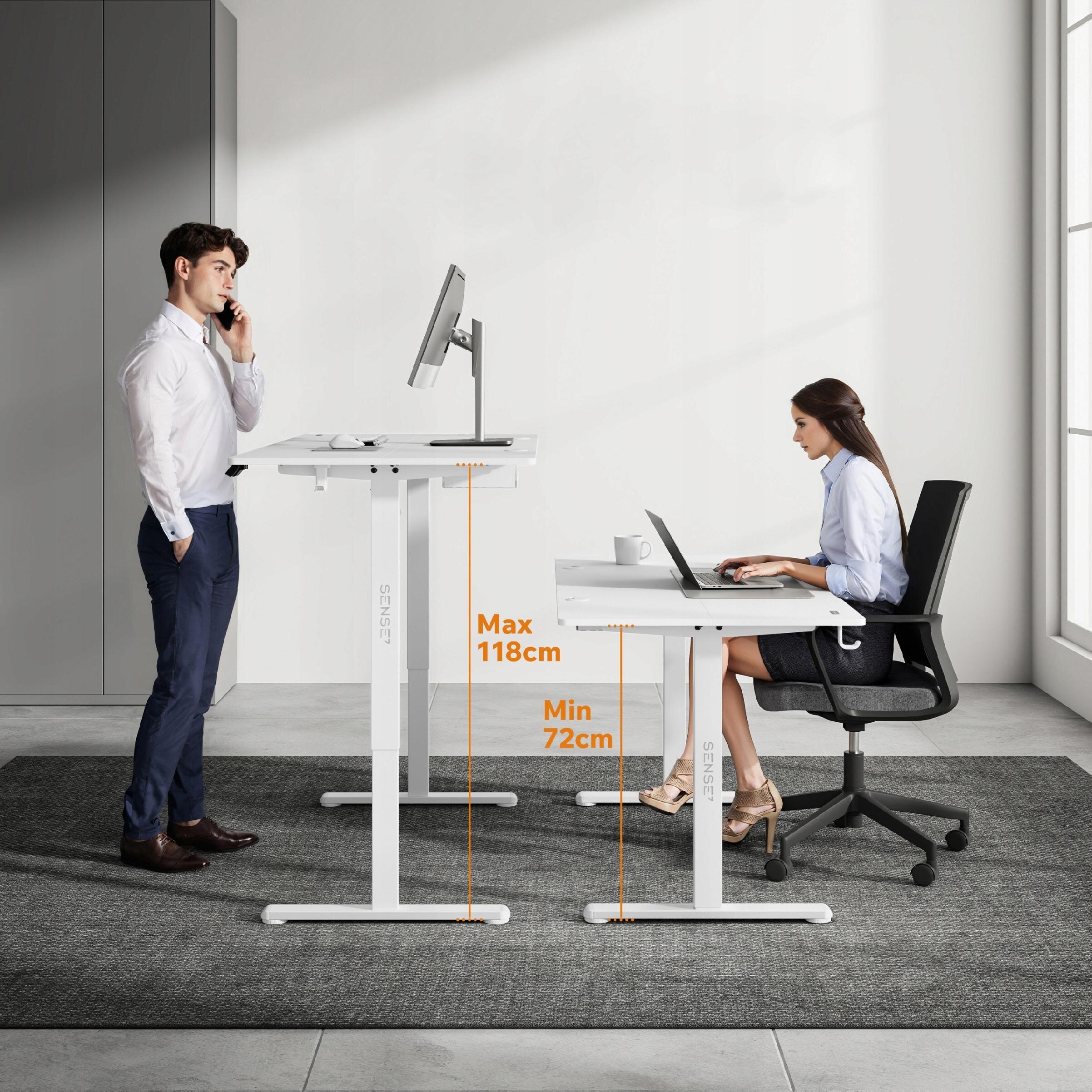 Na obrazie widoczne są dwa biurka z regulacją wysokości, jedno ustawione na wysokości 118 cm, a drugie na 72 cm. Na biurkach znajdują się monitory, a obok nich stoją osoby w biurowym otoczeniu.