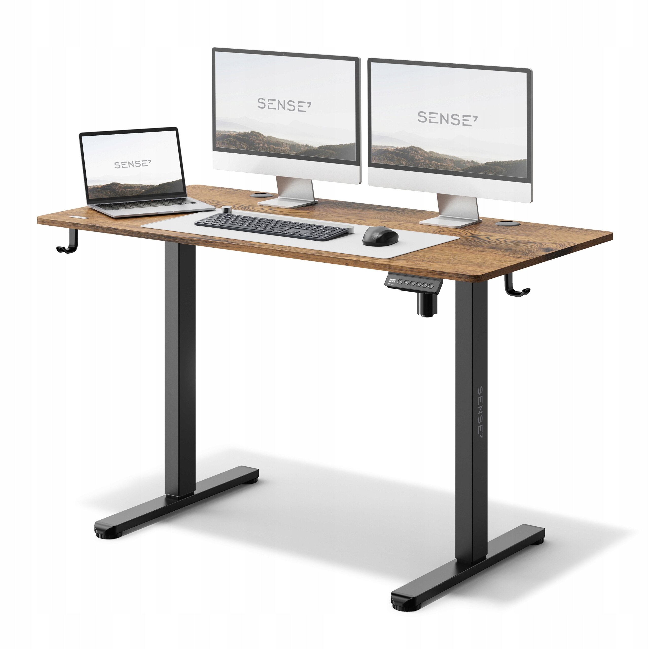 Na obrazie widoczne jest biurko z ciemnobrązowym blatem, na którym znajdują się dwa monitory, laptop, klawiatura i myszka. Na monitorach widnieje logo \'SENSE7\'.