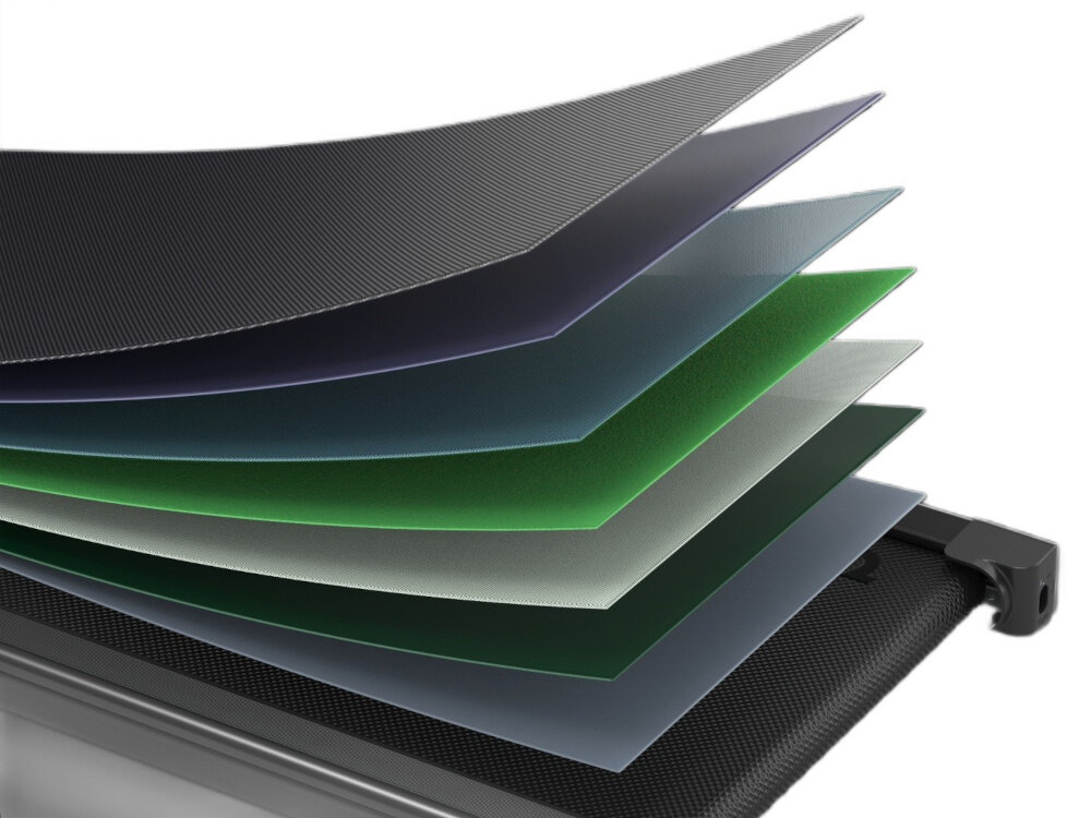 Obraz przedstawia przekrój warstwowy bieżni elektrycznej, ukazujący kilka kolorowych warstw materiału ułożonych jedna nad drugą. Każda warstwa ma inny kolor, w tym odcienie czerni, zieleni i niebieskiego.