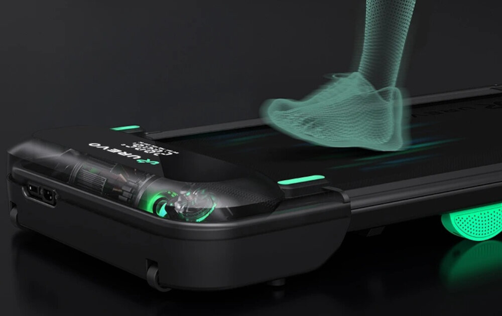 Na obrazie widoczna jest bieżnia elektryczna z wyświetlaczem pokazującym tekst \'UREVO\'. Na bieżni znajduje się przezroczysty model stopy w ruchu.