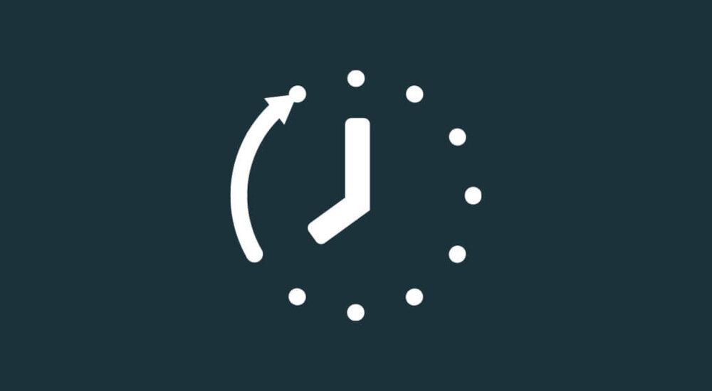 Ikona przedstawia stylizowany zegar z białymi wskazówkami i kropkami na ciemnym tle. Wskazówka godzinowa jest skierowana na godzinę 2, a minutowa na godzinę 12, z zakrzywioną strzałką wskazującą ruch do przodu.