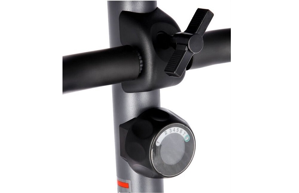 Zbliżenie na element regulacyjny roweru magnetycznego z pokrętłem oznaczonym cyframi od 1 do 8. Widoczna jest także część metalowej ramy z czarnym uchwytem.