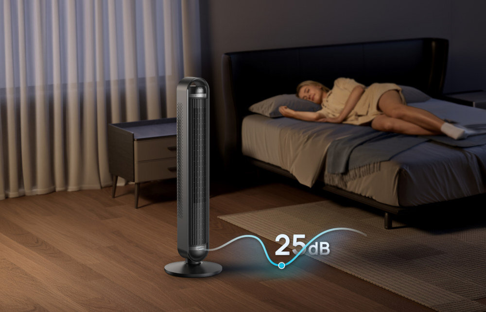 W pokoju znajduje się wentylator kolumnowy obok łóżka, na którym leży osoba. Na obrazie widoczny jest napis \'25 dB\'.