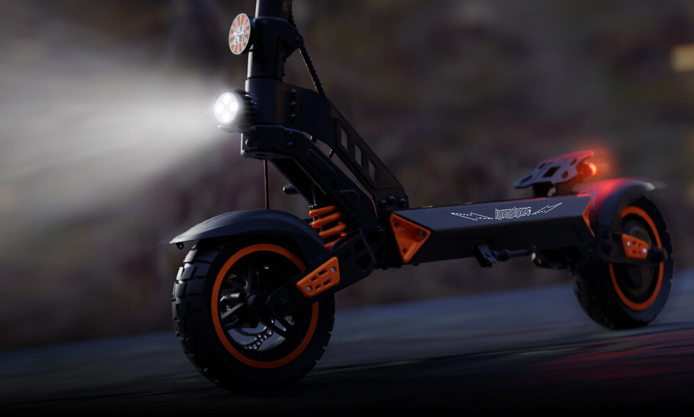 Czarna hulajnoga elektryczna z pomarańczowymi akcentami, wyposażona w przednie i tylne światła oraz amortyzatory. Na boku widoczny jest napis \'KAMIKAZE\'.