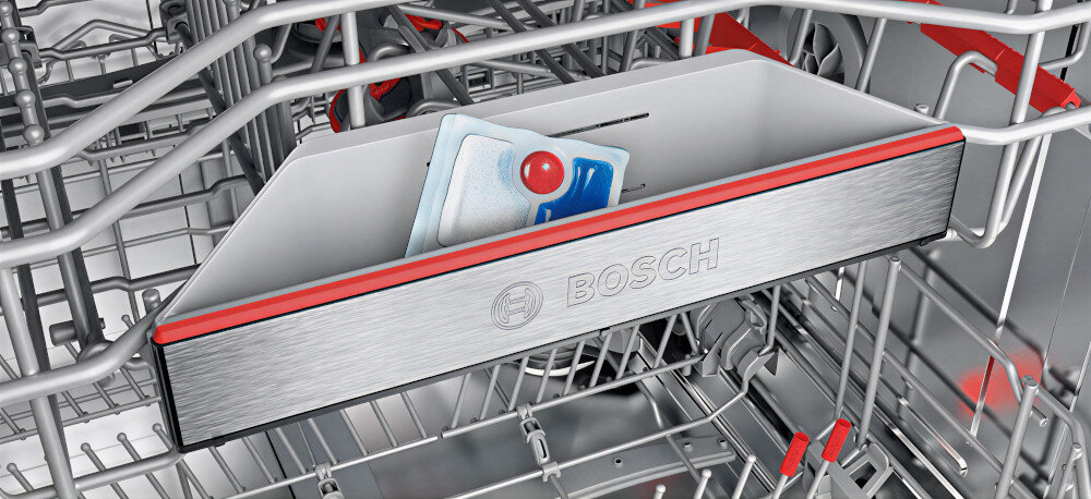 Wnętrze zmywarki z widocznym pojemnikiem na tabletki do mycia, na którym znajduje się logo \'BOSCH\'.