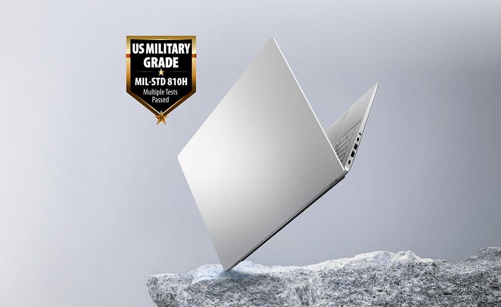 Srebrny laptop unosi się nad powierzchnią przypominającą skałę. Obok widoczny jest emblemat z napisem \'US MILITARY GRADE MIL-STD 810H Multiple Tests Passed\'.