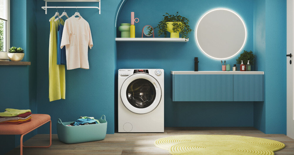 Nowoczesna łazienka z pralką CANDY RapidÓ, otoczona niebieskimi ścianami i meblami. Na półce znajdują się dekoracje, a obok pralki widać kosz z praniem.