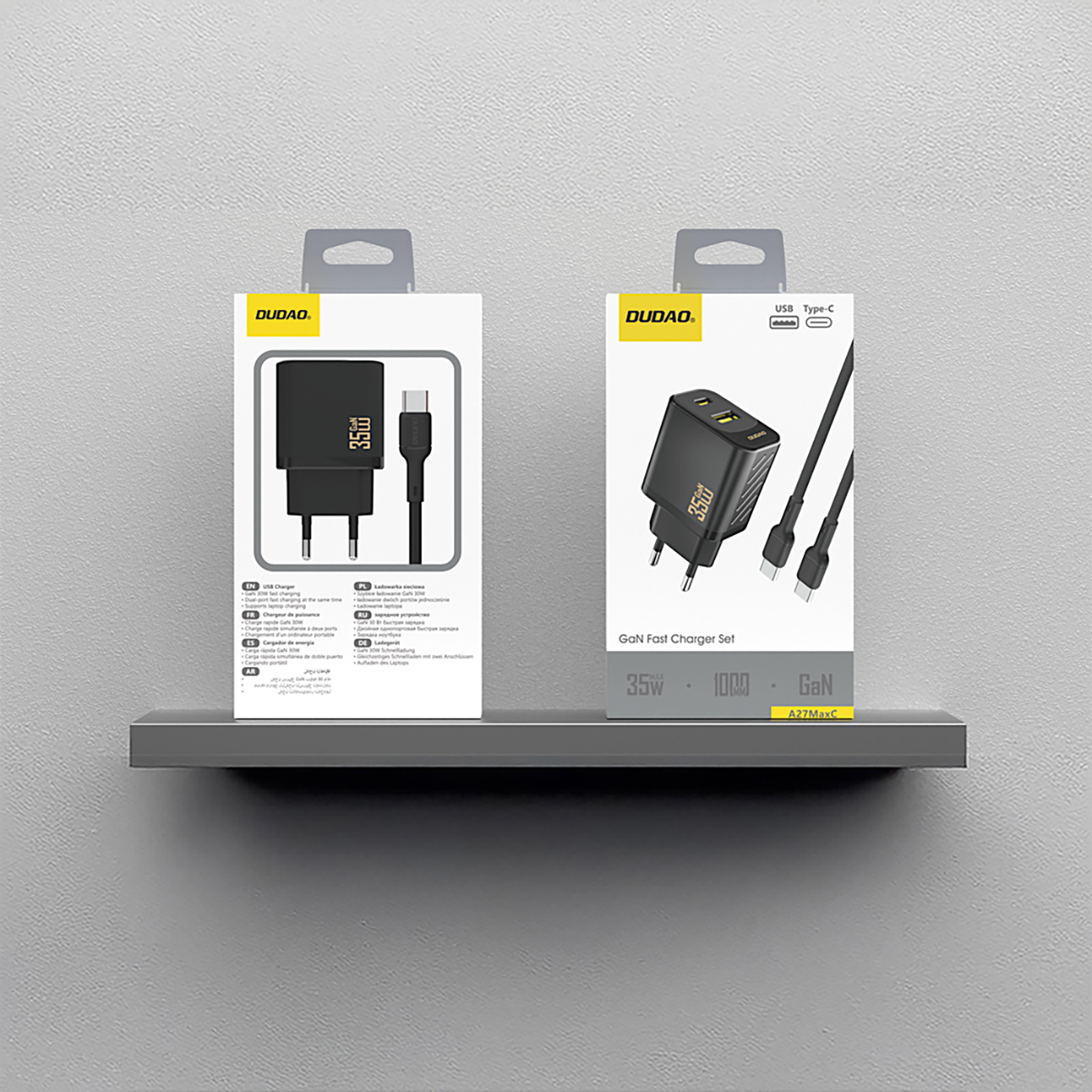 Na obrazie widoczne są dwa opakowania ładowarki sieciowej Dudao z kablem USB-C, umieszczone na półce. Opakowania zawierają ilustracje produktu oraz napisy: \'USB Charger\', \'35W\', \'1000\', \'GaN\', \'A27MaxC\'.