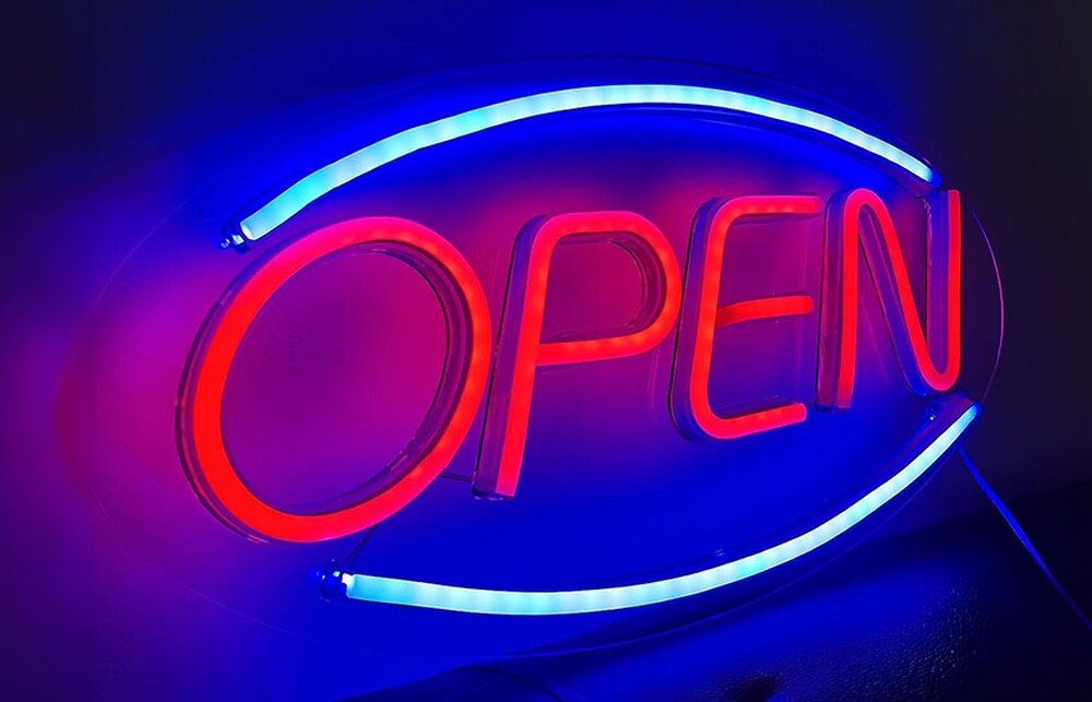 Neonowy napis \'OPEN\' w kolorze czerwonym, otoczony niebieską obwódką, świeci na ciemnym tle.
