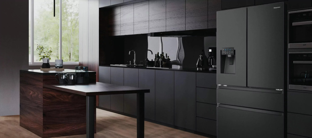 Nowoczesna kuchnia z ciemnymi szafkami i dużą czarną lodówką typu side by side. Na blacie wyspy kuchennej znajdują się czarne naczynia, a przez okno widać zieleń drzew.