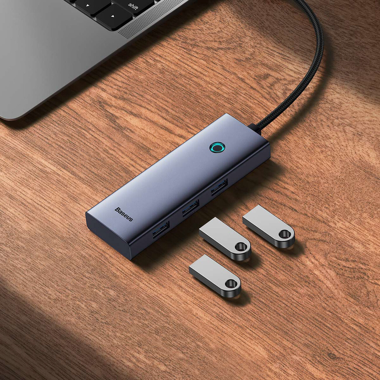Na drewnianym blacie znajduje się kompaktowy hub z logo \'Baseus\', posiadający kilka portów USB-A oraz jeden port HDMI. Obok leżą trzy metalowe adaptery o prostokątnym kształcie.