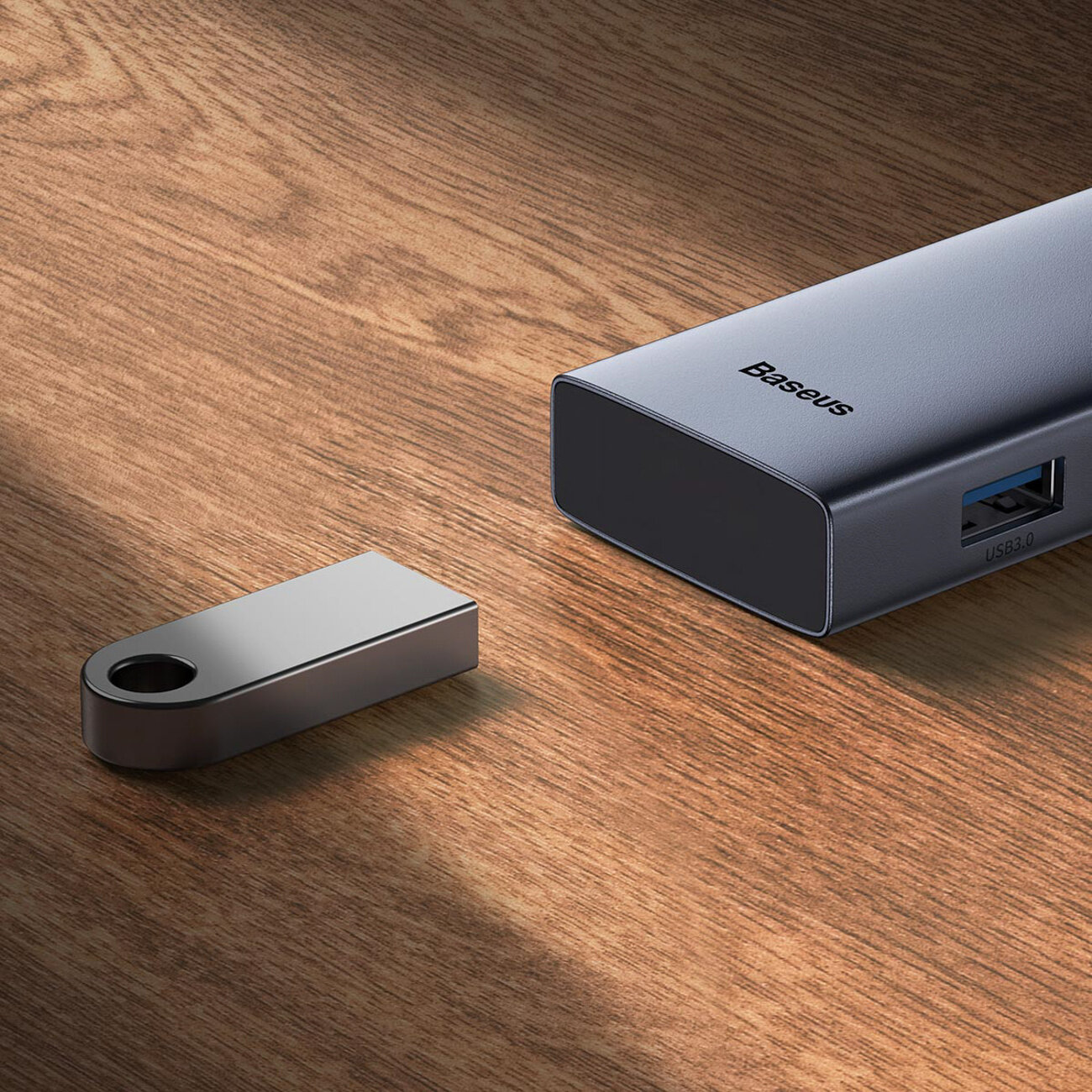 Na drewnianej powierzchni leży kompaktowy hub z logo \'Baseus\' oraz portem USB 3.0. Obok znajduje się metalowy pendrive z otworem na końcu.