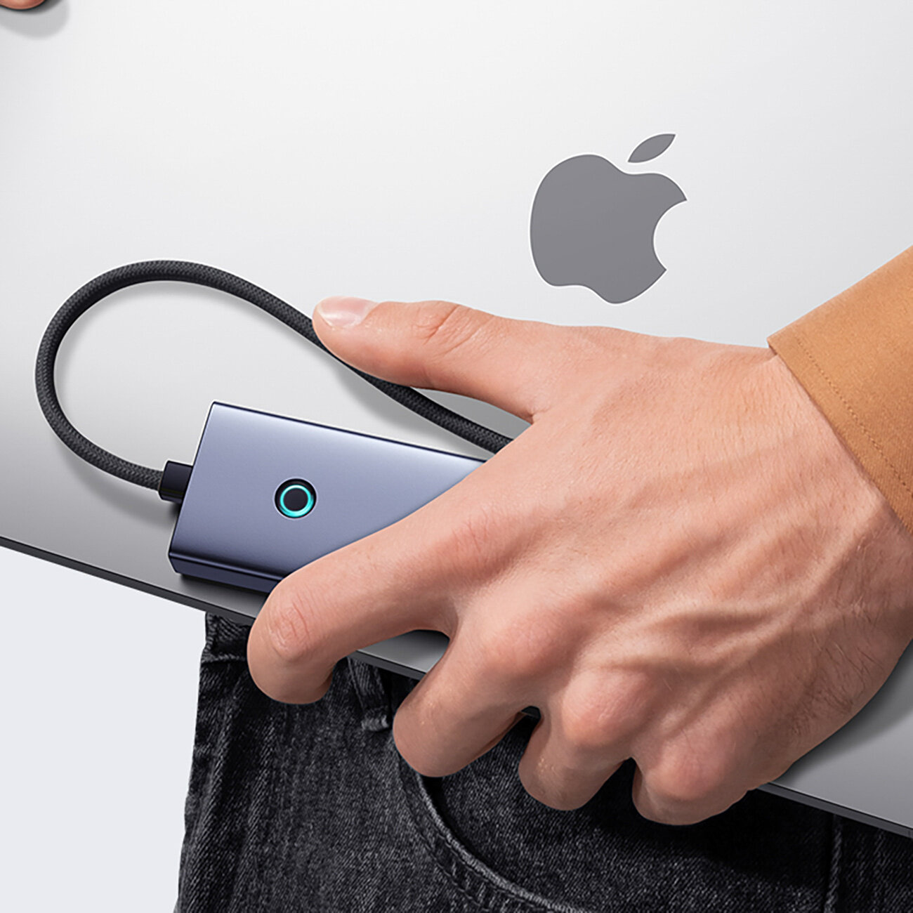 Osoba trzyma kompaktowy hub USB-C z kilkoma portami, podłączony do laptopa z widocznym logo jabłka.