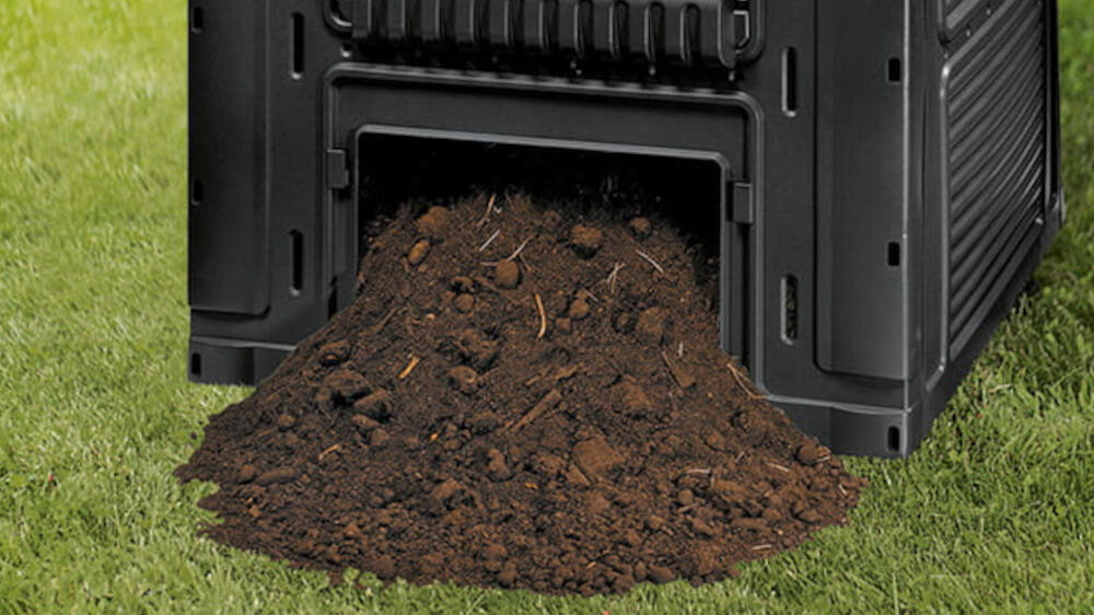 Czarny kompostownik z otwartym dolnym panelem, z którego wysypuje się ziemia na trawę. Kompostownik ma pionowe i poziome żłobienia na powierzchni.
