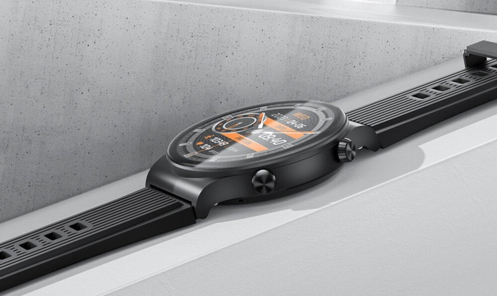 Czarny smartwatch z okrągłą tarczą, wyświetlający kolorowy interfejs z różnymi wskaźnikami i cyframi. Pasek zegarka jest wykonany z tworzywa sztucznego z prostokątnymi otworami.