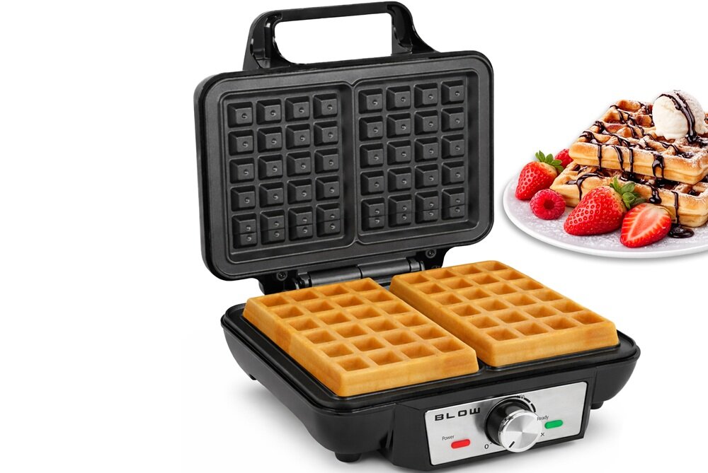 Gofrownica z otwartą pokrywą, w której znajdują się dwa gotowe gofry. Obok widoczny jest talerz z goframi udekorowanymi owocami i polewą, a na urządzeniu znajduje się napis \'BLOW\'.