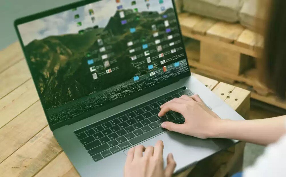 Dysk WD Green SN350 Widok z góry na dłonie osoby piszącej na klawiaturze otwartego laptopa, który stoi na drewnianym stole z palet, konstrukcja, kości pamięci, wytrzymałość