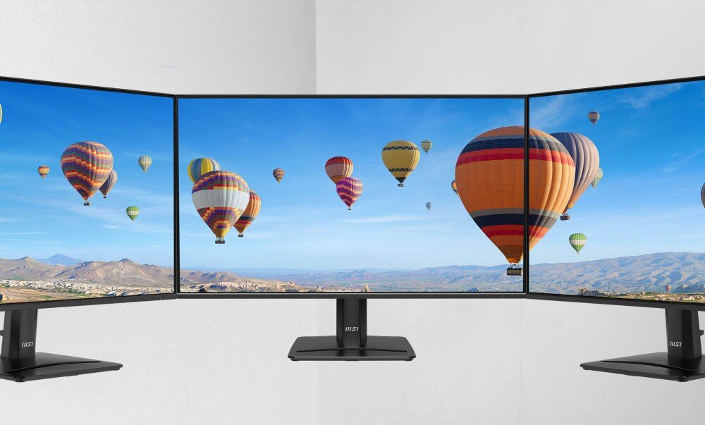 Monitor MSI Pro MP272 E14C Trzy monitory ustawione obok siebie, tworzące jeden szeroki obraz panoramiczny z lecącymi balonami na ogrzane powietrze nad górzystym terenem, ramka, konstrukcja