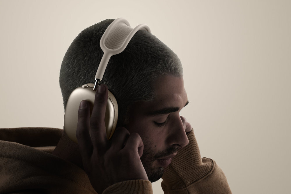Osoba nosi nauszne słuchawki o eleganckim, nowoczesnym designie. Słuchawki mają metaliczne wykończenie i miękkie nauszniki.