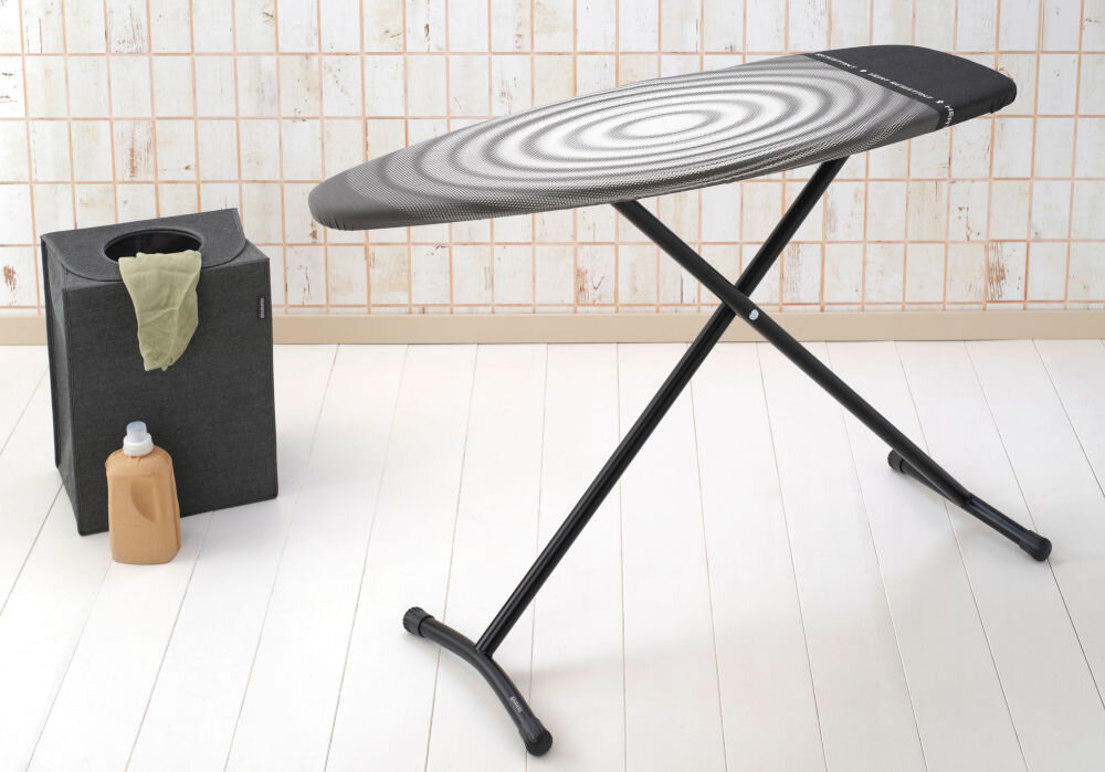 Deska do prasowania BRABANTIA 345647 Titan Oval 135 x 45 cm deska stoi bokiem jasny pokrowiec z czarnymi elementami czarne nóżki jasne tło  certyfikat Cradle-to-Cradle® w poziomie brązowym minimalizowany wpływ na środowisko z materiałów nadających się do recyklingu trwałość łatwość w użytkowaniu ekologiczne rozwiązanie  