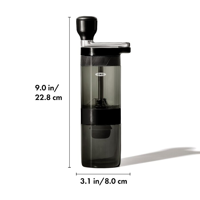 Ręczny młynek do kawy z czarnym uchwytem i przezroczystym pojemnikiem, oznaczony logo \'OXO\'. Wymiary młynka to 9.0 in/22.8 cm wysokości i 3.1 in/8.0 cm szerokości.