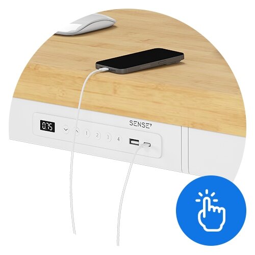 Biurko z bambusowym blatem i białą podstawą, wyposażone w panel sterowania z wyświetlaczem, przyciskami i portem USB. Na blacie leży smartfon podłączony do ładowania.