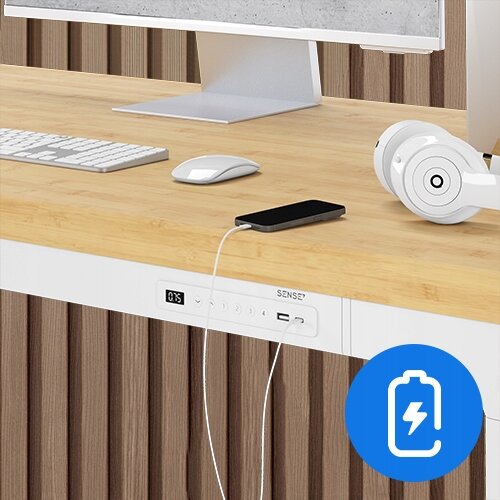 Na obrazie widoczne jest biurko z bambusowym blatem, na którym znajdują się monitor, klawiatura, myszka, słuchawki i smartfon podłączony do ładowania. Na froncie biurka widoczny jest panel z przyciskami i logo \'SENSE7\'.