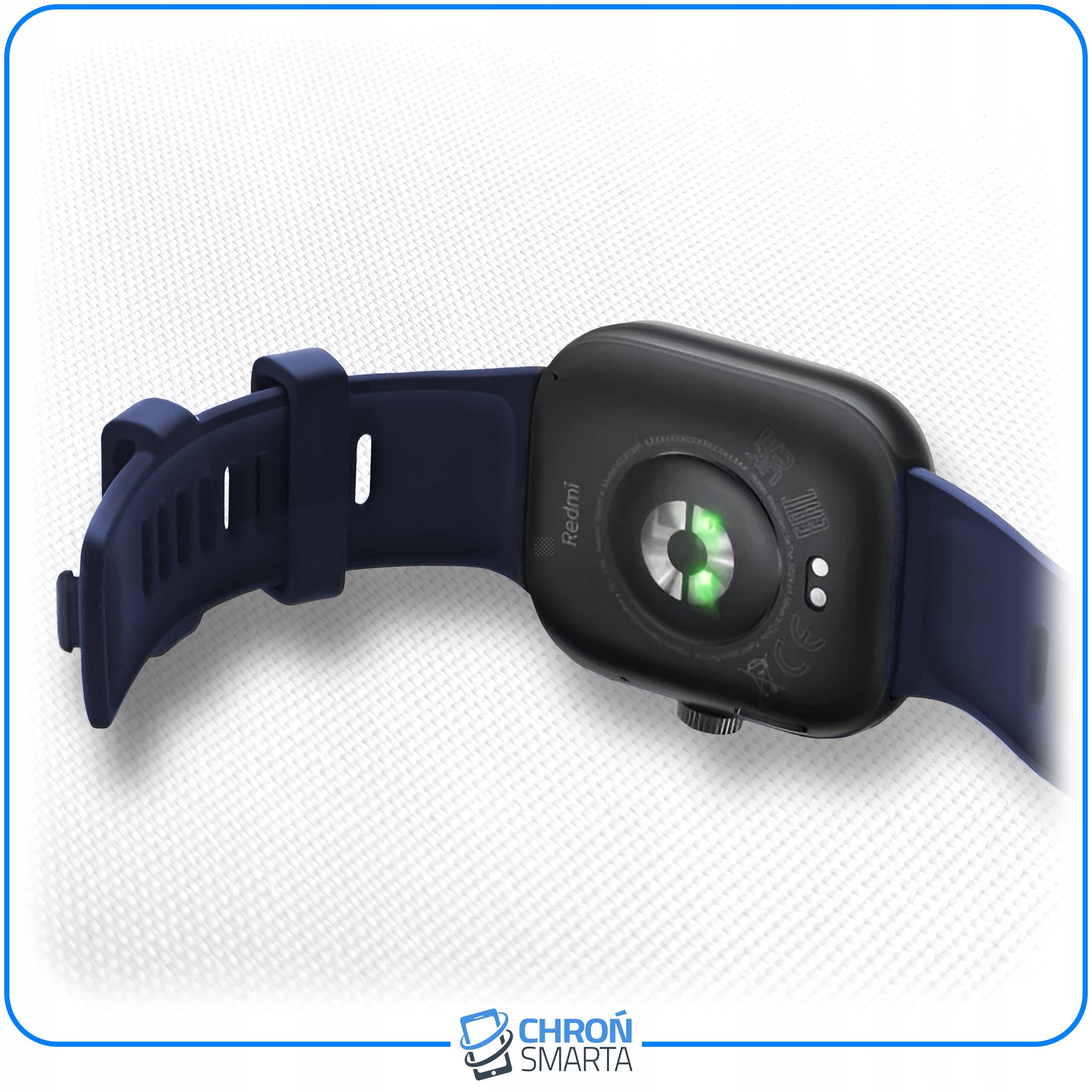 Na obrazie widoczny jest smartwatch z ciemnym paskiem i czarną kopertą, na której znajduje się logo \'Redmi\'. W tle widoczna jest tekstura materiału, a na dole logo \'CHROŃ SMARTA\'.