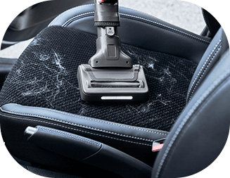 Odkurzacz ręczny czyszczący siedzenie samochodowe pokryte sierścią. Siedzenie jest wykonane z ciemnego materiału z jasnymi włoskami.