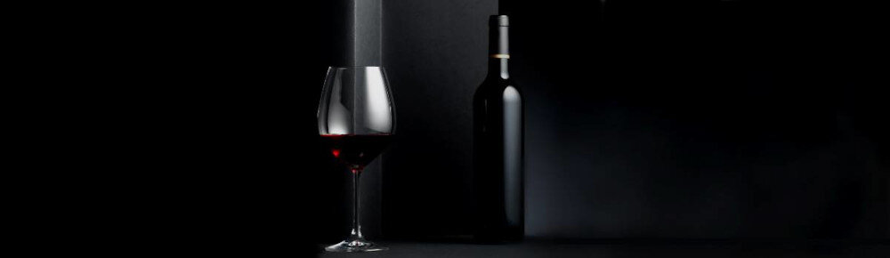 Na obrazie widoczny jest kieliszek z czerwonym winem oraz butelka wina na ciemnym tle. Oba przedmioty są oświetlone delikatnym światłem, tworząc elegancki nastrój.