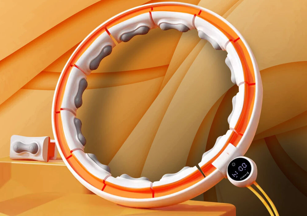 Obraz przedstawia biało-pomarańczowe hula hop z segmentami masującymi wewnątrz. Obok znajduje się mały wyświetlacz z napisem \'1:00\'.