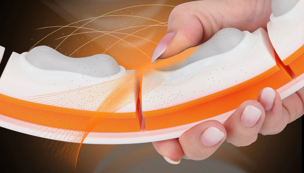 Osoba trzyma segment hula hop w kolorze biało-pomarańczowym z widocznymi wypustkami. W tle widać pomarańczowe linie i efekty świetlne.