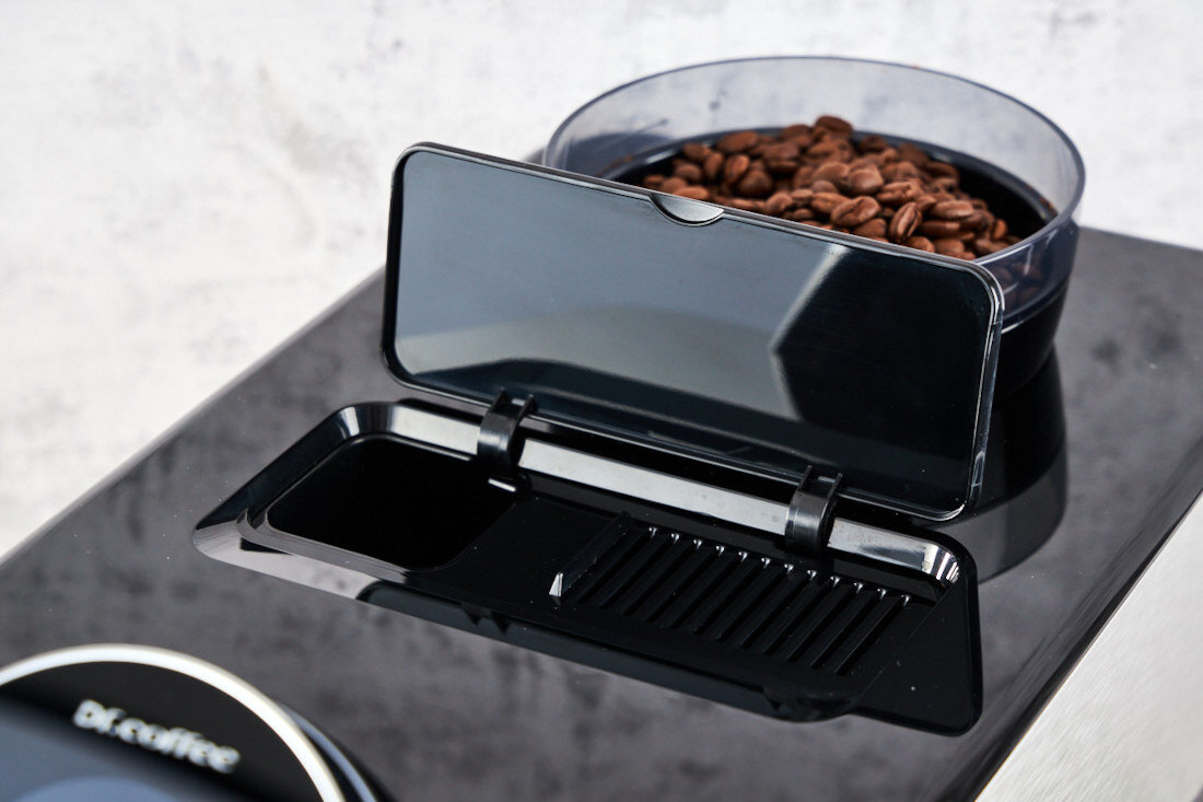 Na zdjęciu widoczny jest ekspres do kawy z otwartym pojemnikiem na ziarna kawy. Na urządzeniu znajduje się logo \'Dr.Coffee\'.
