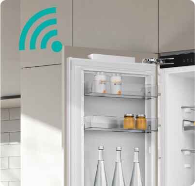 Otwarta lodówka z widocznymi półkami, na których znajdują się butelki i słoiki. W lewym górnym rogu widoczny jest symbol Wi-Fi.