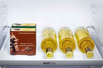 W lodówce na półce znajdują się trzy butelki z żółtym płynem oraz pudełko z napisem \'MILK CHOCOLATE 40%\'. Na półce widoczny jest napis \'Multi Tray\'.