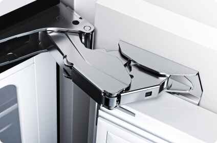 Zdjęcie przedstawia chromowany zawias drzwiowy zamontowany na białej powierzchni. Zawias jest masywny i ma nowoczesny design.