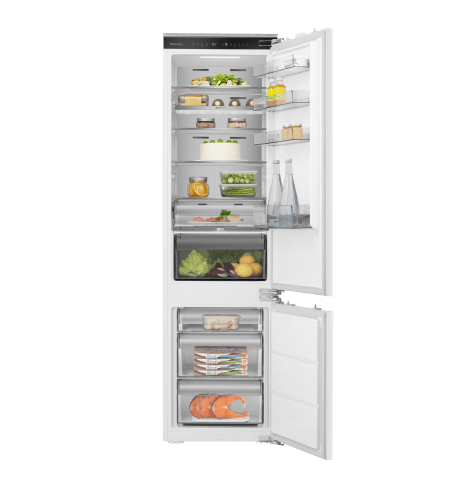 Otwarta lodówka z widocznymi półkami wypełnionymi różnymi produktami spożywczymi, takimi jak warzywa, napoje i nabiał. Drzwi lodówki również mają półki z dodatkowymi produktami.