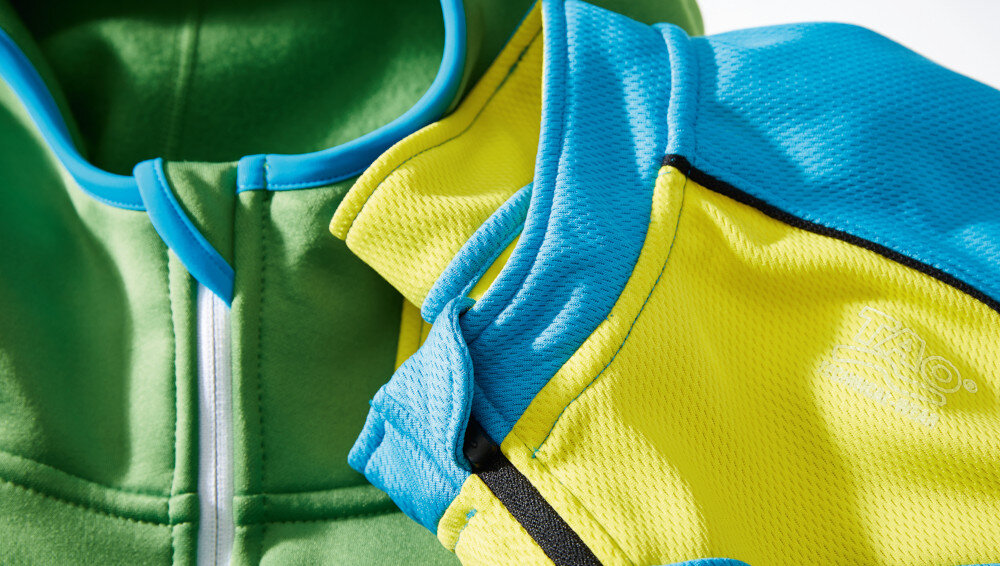 Kolorowe tkaniny w odcieniach zieleni, żółci i niebieskiego z widocznym zamkiem błyskawicznym. Na żółtej tkaninie widoczny jest napis \'Tao\'.