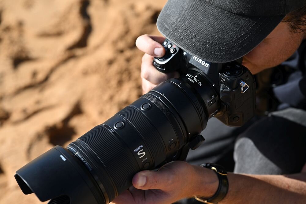 Osoba trzyma aparat fotograficzny z obiektywem marki Nikon, na którym widoczne są napisy \'NIKKOR Z 70-200mm f/2.8 VR S\'.