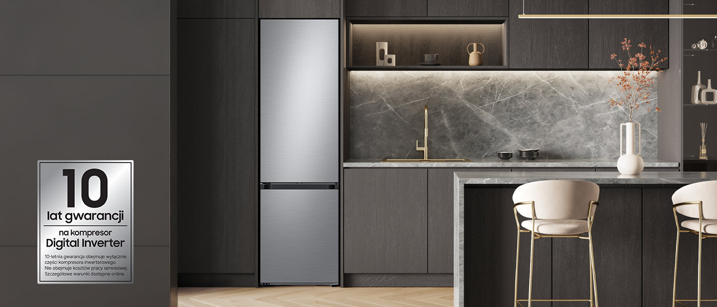 Kuchnia z nowoczesną lodówką w kolorze szczotkowanej stali nierdzewnej, obok której znajduje się marmurowy blat z krzesłami. Na ścianie widoczny jest napis: \'10 lat gwarancji na kompresor Digital Inverter\'.