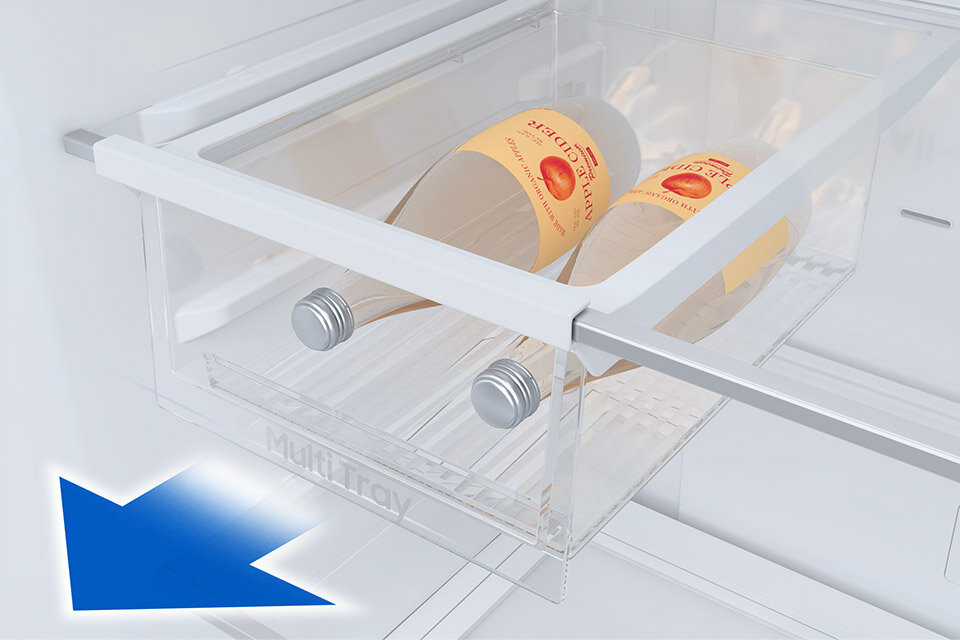 Wysuwana taca Wnętrze lodówki z przezroczystą szufladą oznaczoną napisem \'Multi Tray\', w której znajdują się dwie butelki z etykietą przedstawiającą owoc. W dolnym rogu widoczna jest niebieska strzałka skierowana w dół.