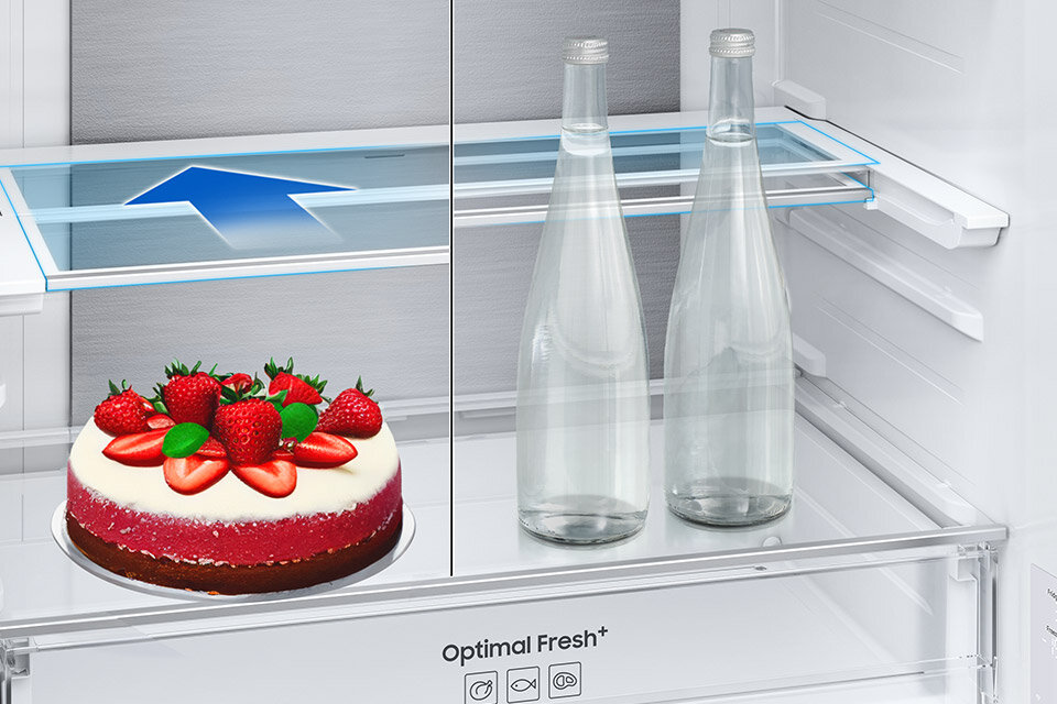 Składana półka Wnętrze lodówki z widocznymi dwoma szklanymi butelkami i tortem ozdobionym truskawkami na półce. Na szufladzie znajduje się napis \'Optimal Fresh+\'.
