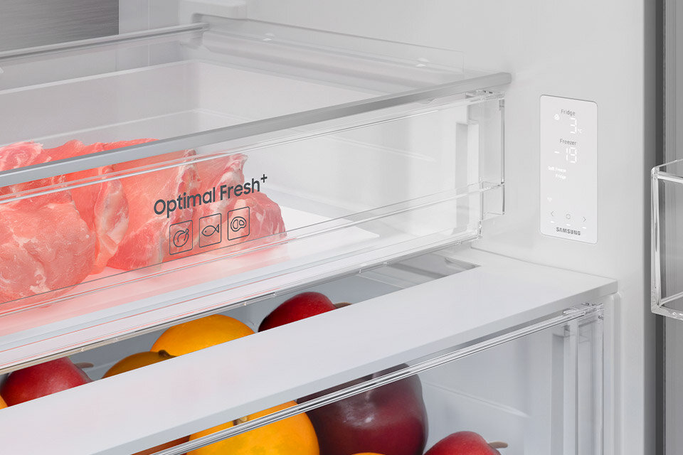 Wnętrze lodówki z przezroczystymi szufladami, w jednej z nich znajduje się mięso z napisem \'Optimal Fresh+\'. Obok widoczny jest panel z wyświetlaczem temperatury i logo Samsung.