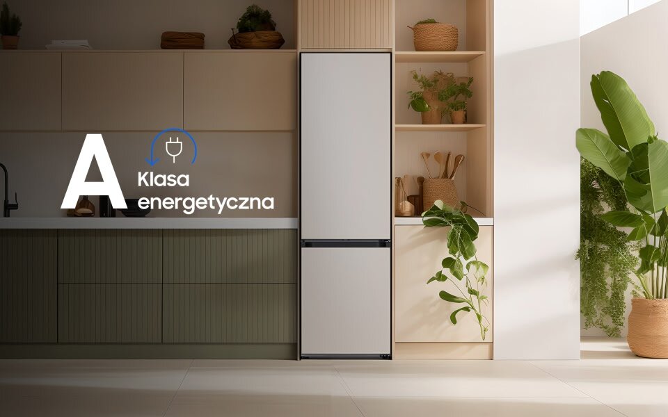 Lodówka w kolorze beżowym stoi w nowoczesnej kuchni z roślinami i drewnianymi elementami. Na obrazie widoczny jest tekst: \'A Klasa energetyczna\'.