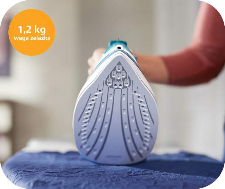 Zdjęcie przedstawia żelazko z widoczną stopą z otworami parowymi, trzymane przez osobę. W lewym górnym rogu znajduje się pomarańczowe kółko z tekstem \'1,2 kg waga żelazka\'.